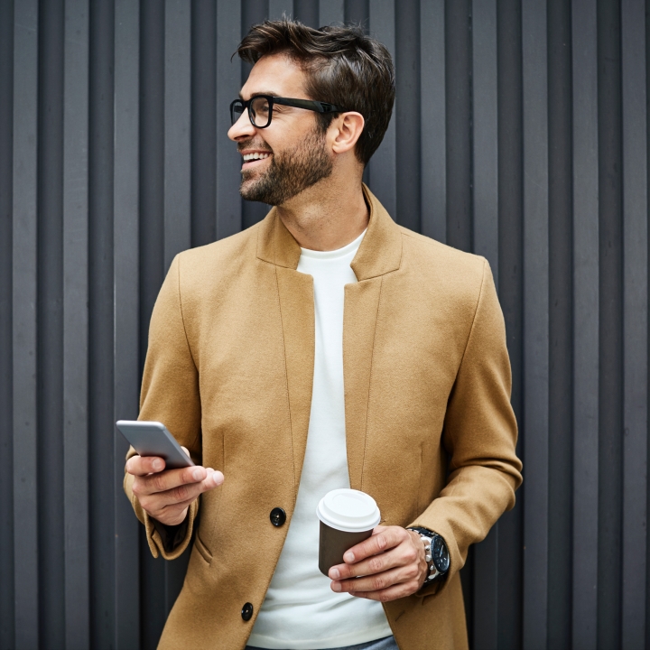 man with glasses holding a mobile phone and a coffee